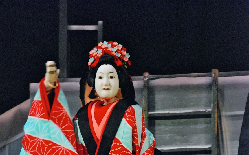 Close view of a bunraku puppet of a young woman with flowered hairpins, in a red and pale blue kimono