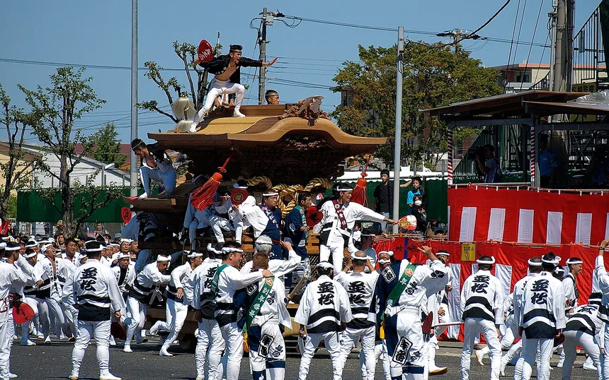 A team in white pulling a carved danjiri float through a Kishiwada street, with a carpenter riding the roof; photographed at the September festival