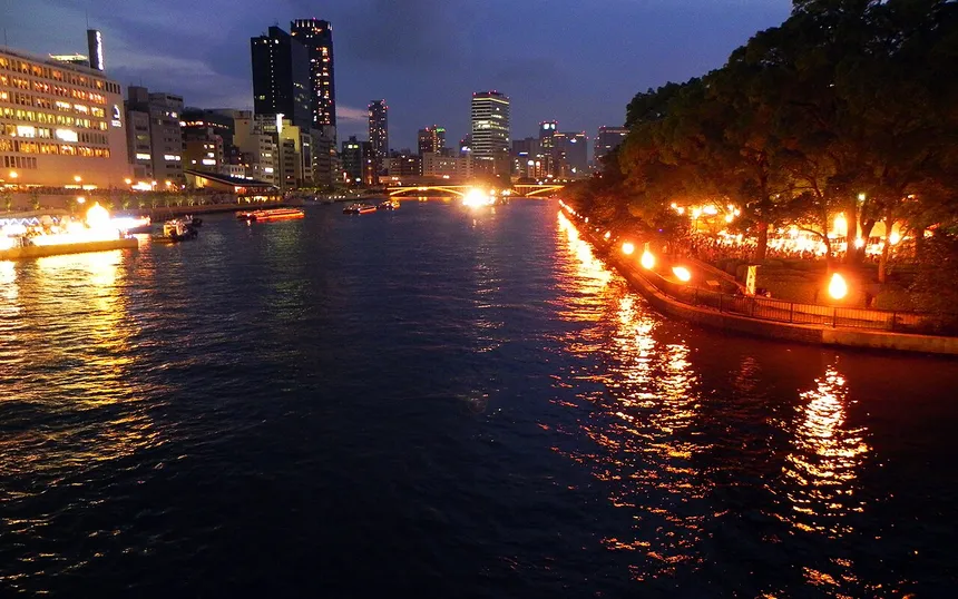 Bonfires along the bank and boats on the Okawa river at dusk during Tenjin Matsuri
