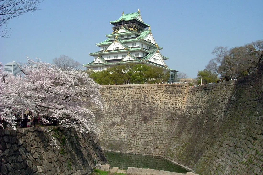 The keep of Osaka Castle above the stone walls of the moat, with cherry trees in bloom